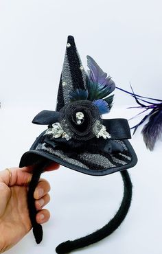 This Witch Hat Fascinator is an easy and classy way to dress up this year! This is a black and silver witch hat that is attached to a black yarn wrapped headband. The hat is adorned with ruffled lace, a netted flower, rhinestones and iridescent feathers. Will Fit a 4 year old and up! Like our Facebook Page and get 10% off when you message me before checkout! Everything made by handmade MKE is one of a kind and unique, however, if you would like a different size or see a piece that you would like Novelty Brimmed Costume Accessories For Party, Novelty Brimmed Costume Accessories For Costume Party, Halloween Wide Brim Fitted Mini Hat, Novelty Costume Hats And Headpieces For Parties, Novelty Party Costume Hats And Headpieces, Fitted Wide Brim Mini Hat For Halloween, Whimsical Adjustable Costume Hats For Carnival, Whimsical Adjustable Costume Hats And Headpieces For Carnival, Curved Brim Costume Hats And Headpieces