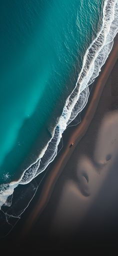 an aerial view of the ocean and beach with waves coming in from the water, taken from above