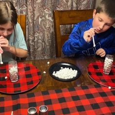 two children sitting at a table eating marshmallows