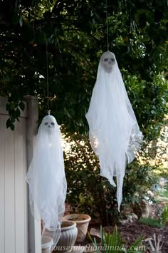 two white ghost decorations hanging from a tree