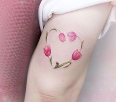 a heart shaped tattoo with pink tulips on the left side of the arm