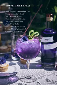 a purple drink sitting on top of a table next to cupcakes and bottles