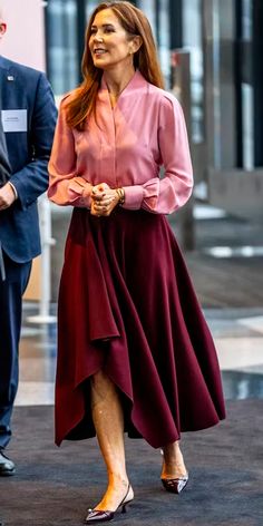 a woman in a pink shirt and maroon skirt is walking down the street with two men behind her