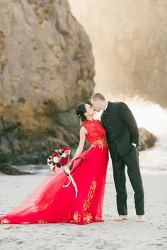 a man and woman in formal wear kissing on the beach with waves crashing behind them