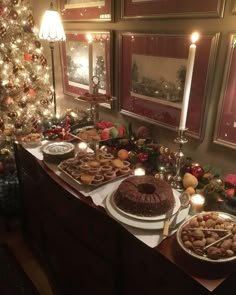 a table topped with lots of food next to a christmas tree and lite candles