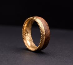 a gold ring with an intricate design on the outside and inside, sitting on a black surface