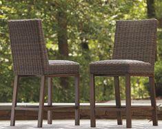 two brown wicker chairs sitting next to each other on top of a stone floor