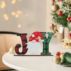 a wooden joy sign sitting on top of a white table next to a christmas tree