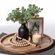 a wooden tray topped with a vase filled with flowers next to a candle and photo frame