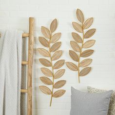 two wooden leaves are hanging on the wall next to a ladder and pillows in front of a white brick wall