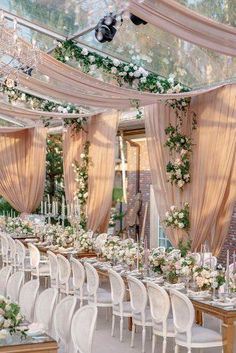 an outdoor wedding reception setup with white chairs and flowers on the tables, along with greenery