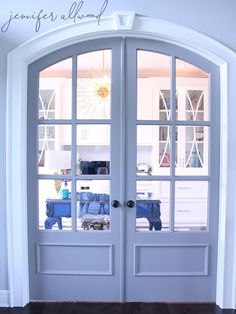 an open double door leading into a kitchen with white walls and wood floors, in front of a doorway that has glass panes on both sides