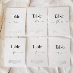 four place cards with calligraphy on them sitting on a white sheeted bed spread