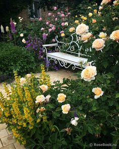 a white bench sitting in the middle of a garden filled with pink and yellow flowers