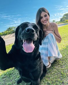 a woman sitting in the grass with her black dog and holding it's paw up