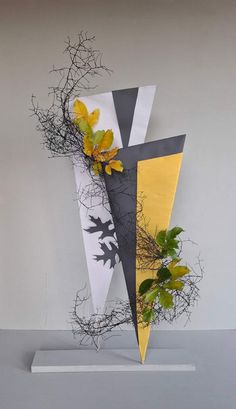 a sculpture with yellow and black leaves on it's sides, in front of a gray wall