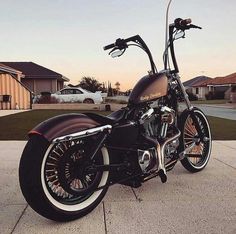 a black motorcycle parked on top of a sidewalk next to a house with cars in the background