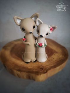 two small figurines are standing on a wooden stand with flowers in their hair