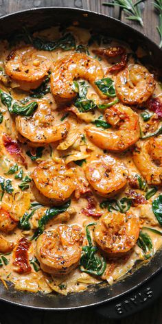 a skillet filled with shrimp and spinach on top of a wooden table,