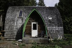 a small house with a green roof and white door in the middle of some trees