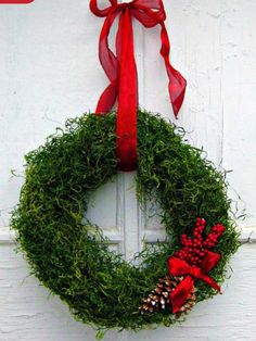 a green wreath with red ribbon hanging on a white door