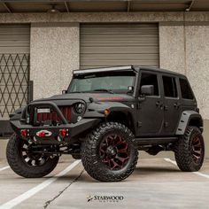 a black jeep is parked in front of a building with red rims and tires