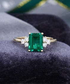 an emerald and diamond ring sitting on top of a velvet cushion