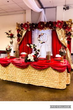 a red and gold wedding table with flowers on it's side, surrounded by white drapes