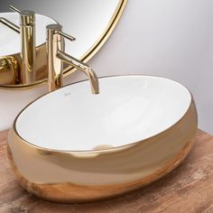 a bathroom sink with a gold faucet and round mirror on the wall behind it