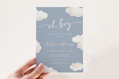 a person holding up a blue and white wedding card with clouds in the sky on it