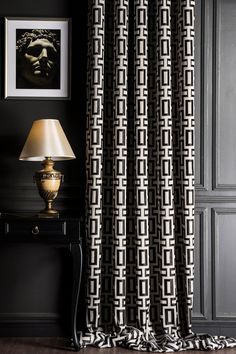 a black and white patterned curtain hanging in front of a table with a lamp on it