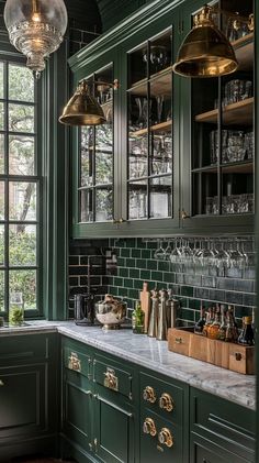 a kitchen with dark green cabinets and marble counter tops, hanging lights above the sink