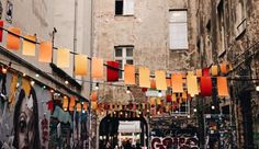 an alleyway with lots of graffiti on the walls and colorful flags hanging above it