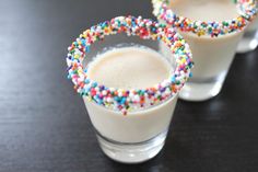 two glasses filled with milk and sprinkles on top of a black table