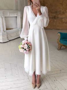 a woman in a white dress taking a selfie with her cell phone while holding a flower bouquet