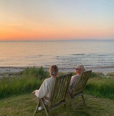 two people sitting on lawn chairs looking out at the ocean and sunset over the water