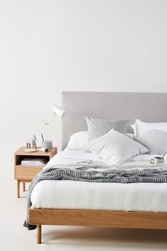 a bed with white sheets and pillows on top of it next to a night stand