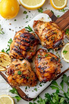 grilled chicken with lemons and parsley on a cutting board next to sliced lemons