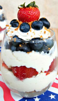 a dessert with strawberries, blueberries and whipped cream in a glass on top of an american flag napkin