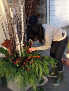 a woman bending over to pick up some leaves from a planter in front of a house