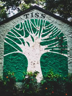 a green and white building with a tree on it's front wall, surrounded by trees