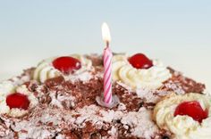 a birthday cake with frosting and cherries has a single candle on it's top