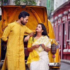 a man standing next to a woman sitting in the back of a yellow car on a city street