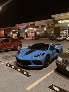 two blue sports cars parked next to each other in front of a building at night