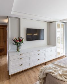 a bedroom with white furniture and a large flat screen tv mounted on the wall above it