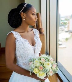 a woman in a wedding dress holding a bouquet and looking out a window at the ocean