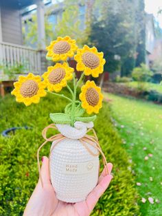 a hand holding a vase with sunflowers in it and tied up to the top