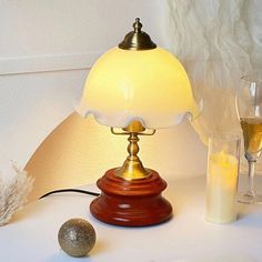 a table lamp sitting on top of a white table next to a glass of wine