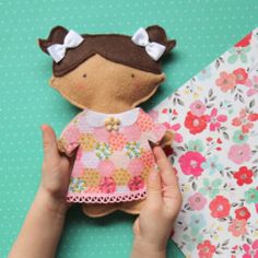 a hand holding a small doll next to a flowered paper and fabric wallpaper