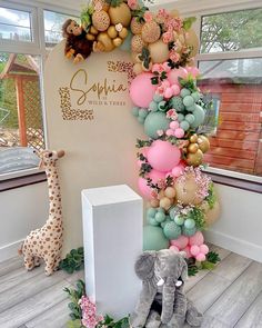 an elephant and giraffe are sitting in front of a wall with balloons on it